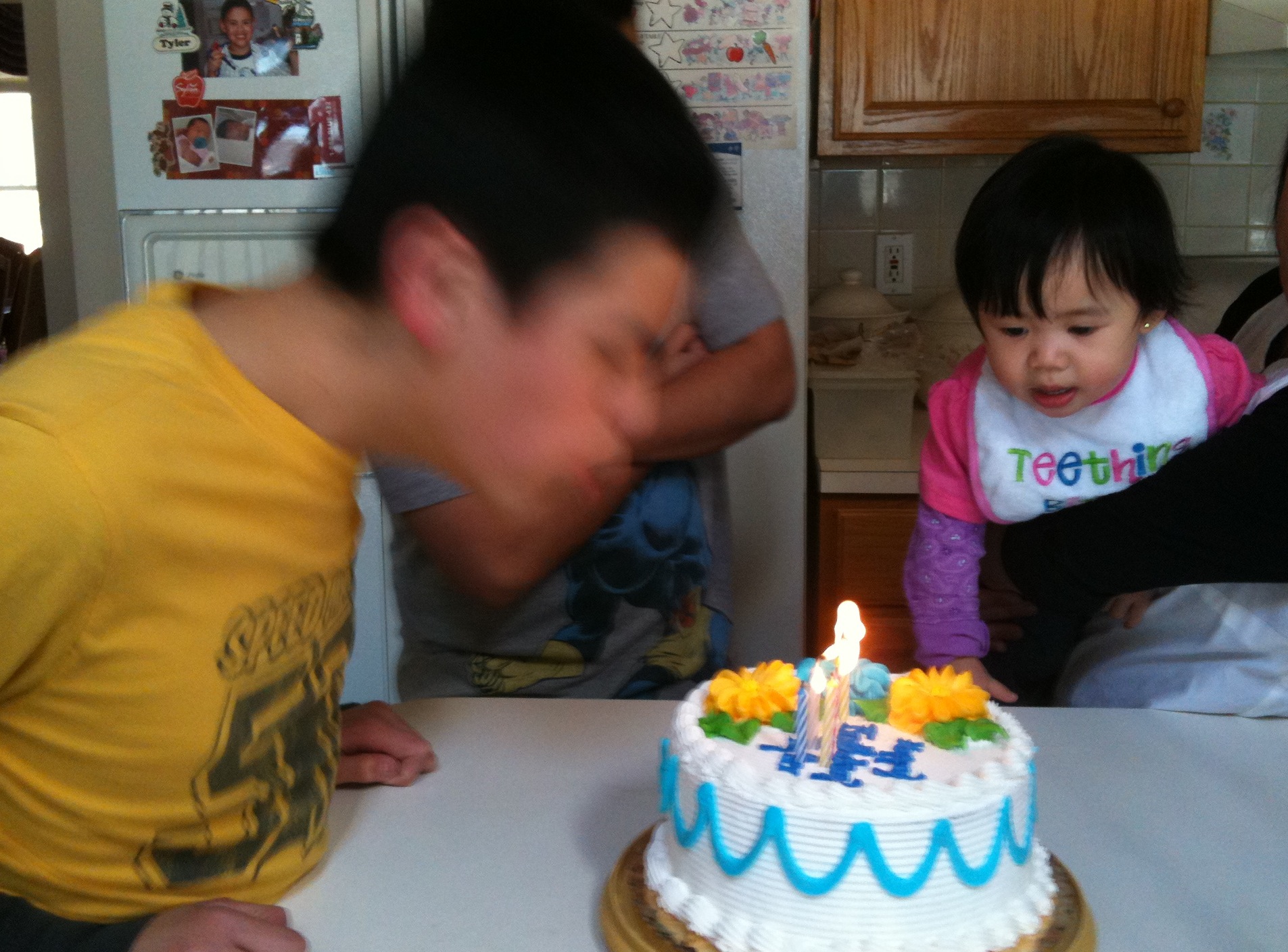 Brother blows out cake, while baby sister watches